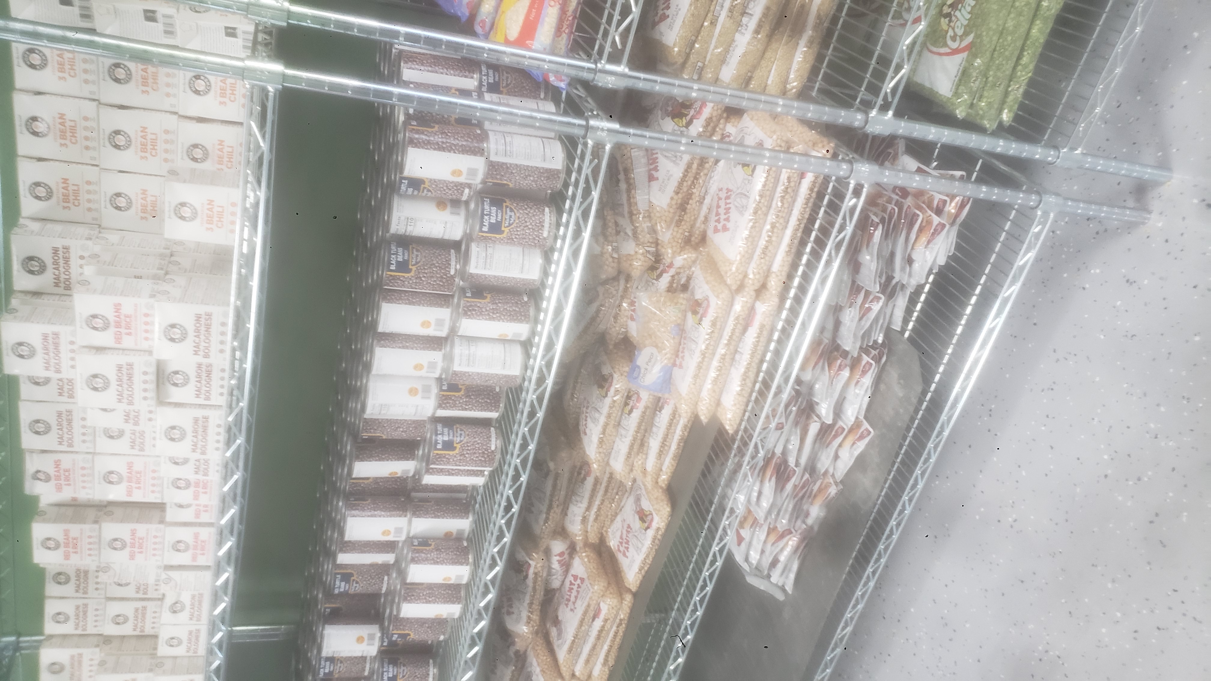 Ready to eat meals, cans of black turtle beans, bags of chickpeas, and pouches of chicken on racks of a shelf.